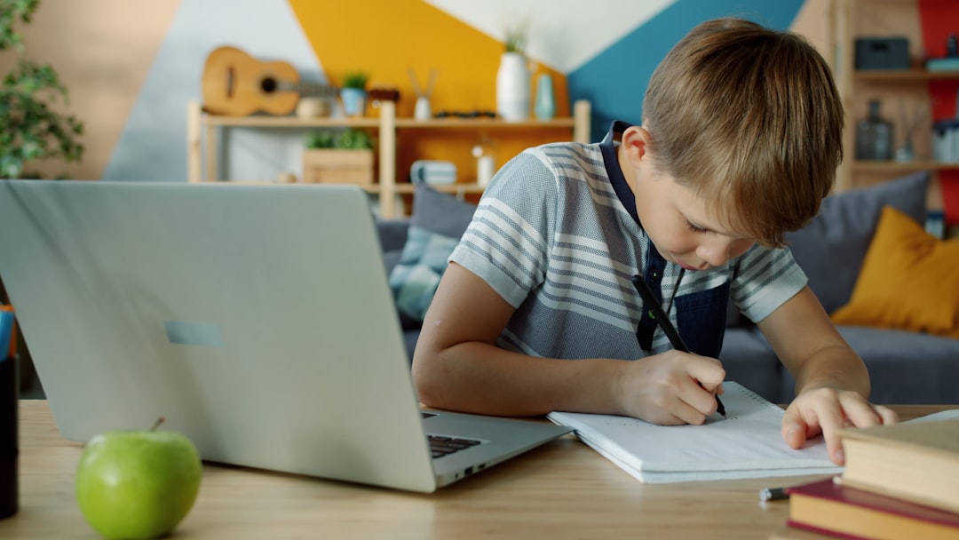 Estudiante de primaria haciendo tareas online con ordenador portátil y cuaderno